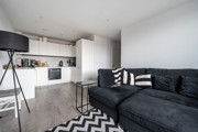 Open-plan living area with corner sofa, floor lamp and adjoining kitchen.