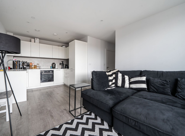 Open-plan living area with corner sofa, floor lamp and adjoining kitchen.