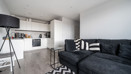 Open-plan living area with corner sofa, floor lamp and adjoining kitchen.