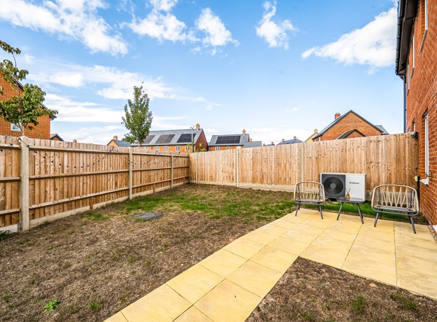 Rear garden with paved patio, airsource heat pump, lawn and fenced boundaries.