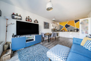 Living room with sofa, television, shelving and dining table, leading into kitchen.