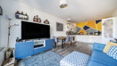 Living room with sofa, television, shelving and dining table, leading into kitchen.