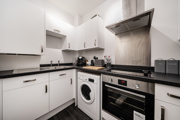 Kitchen with integrated appliances, white units, and tiled backsplash.