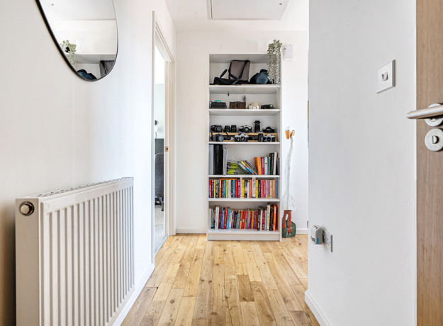 Hallway with wood-effect floor, radiator, and shelving unit.