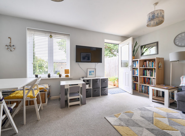 Living room with sofa, TV unit, dining table and doors opening to the garden.