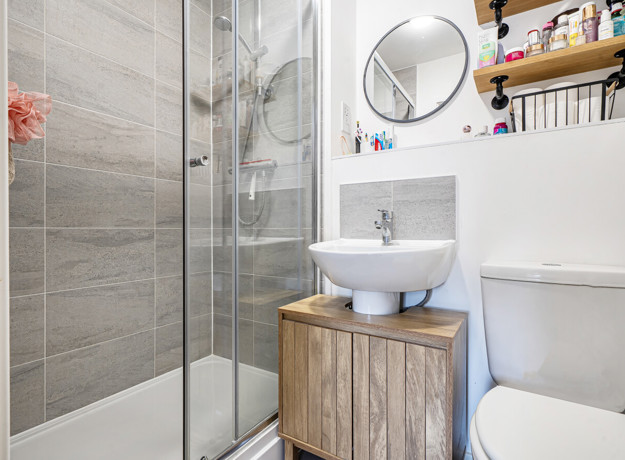 Ensuite with shower enclosure, sink, toilet, and wall shelf.
