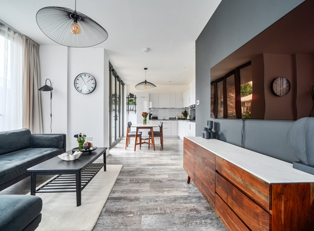 Open-plan living area with sofa and media unit, leading into kitchen.