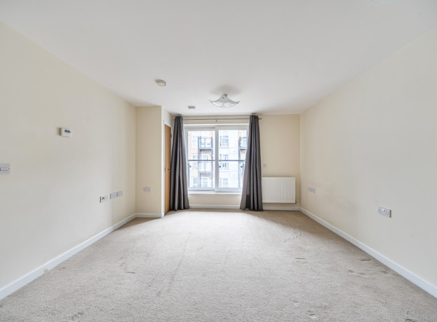 Empty bedroom with window, curtains and wall-mounted radiator.