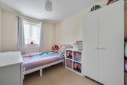 Child's bedroom with single bed, wardrobe, shelving, and window with curtains.