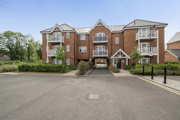 Modern brick apartment building with pitched roofs, entrance doors, and parking area.