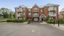 Modern brick apartment building with pitched roofs, entrance doors, and parking area.