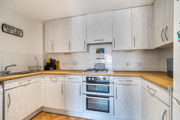 L-shaped kitchen with light cabinetry, tiled splashback, electric cooker, and wood-effect countertops.
