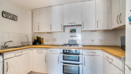 L-shaped kitchen with light cabinetry, tiled splashback, electric cooker, and wood-effect countertops.