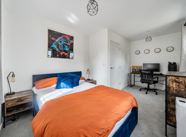 Bedroom with double bed, desk, chair and wall artwork.