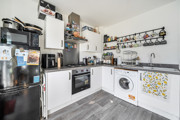 Kitchen with fitted units, oven, washing machine, fridge-freezer and wall shelving.