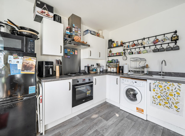 Kitchen with fitted units, oven, washing machine, fridge-freezer and wall shelving.