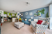 Open-plan living area with armchairs, sofa and breakfast bar leading into kitchen.