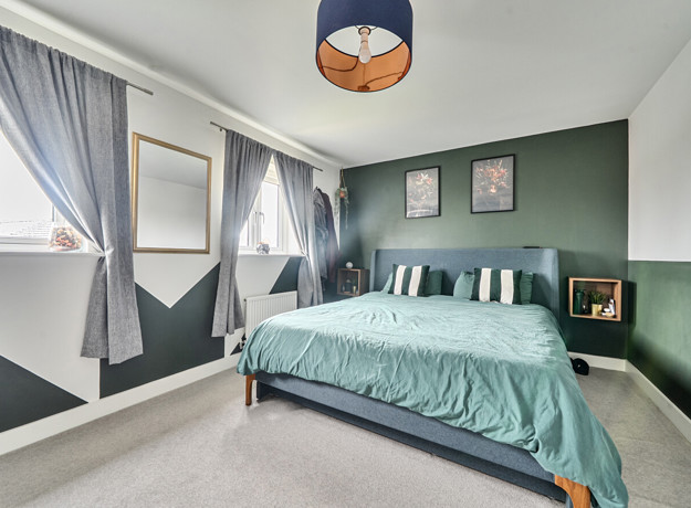 bedroom with double bed, bedside tables, green wall and window with curtains.