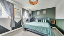 bedroom with double bed, bedside tables, green wall and window with curtains.