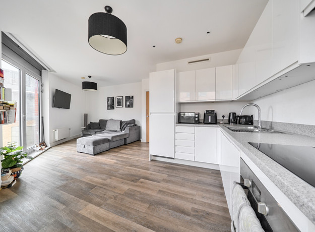 Open-plan living area with kitchen, sofa and large windows.