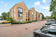 Modern apartment building with hedges, street and parked cars in front.