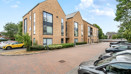 Modern apartment building with hedges, street and parked cars in front.
