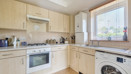 Kitchen with cabinets, oven, sink, boiler, washing machine and window.