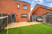 Fenced rear garden with lawn, patio, wooden shed and red brick house.