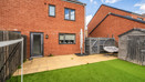 Fenced rear garden with lawn, patio, wooden shed and red brick house.