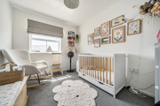 Nursery room with cot, armchair, rug, and framed pictures on the wall.