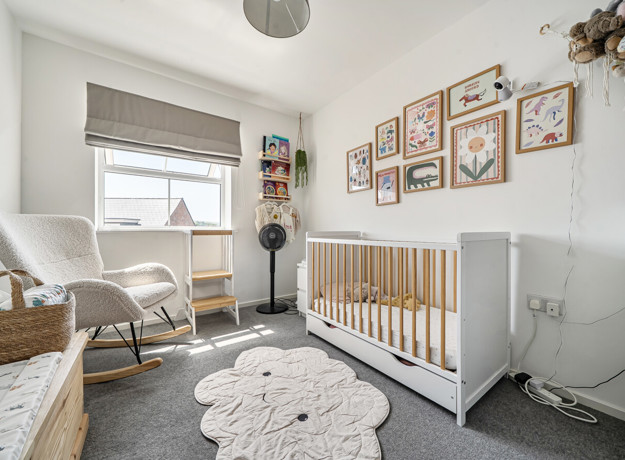 Nursery room with cot, armchair, rug, and framed pictures on the wall.
