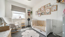 Nursery room with cot, armchair, rug, and framed pictures on the wall.
