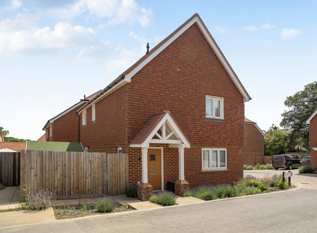 Red brick detached house with driveway, white trim, and fenced front garden.