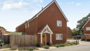 Red brick detached house with driveway, white trim, and fenced front garden.