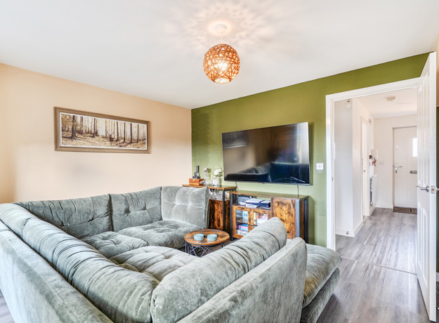 Living room with corner sofa, TV, feature wall and doors into hallway.
