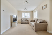 Living room with beige sofas, carpet, television, and windows letting in light.
