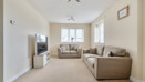 Living room with beige sofas, carpet, television, and windows letting in light.