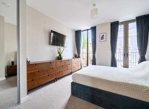 Bedroom with double bed, wall-mounted TV, storage unit and balcony doors.