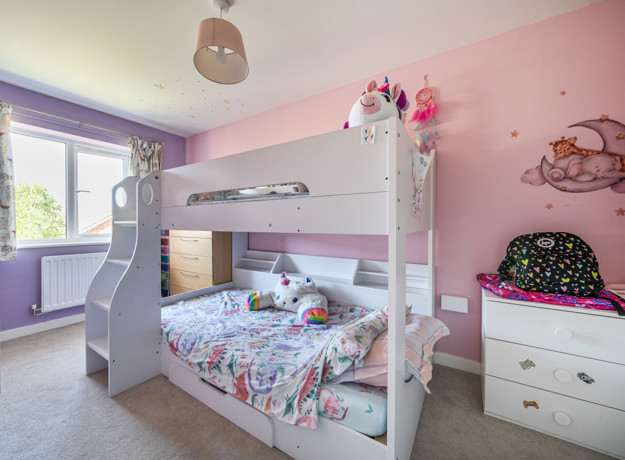 Children’s bedroom with white bunk bed, pink walls, and storage furniture.