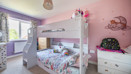 Children’s bedroom with white bunk bed, pink walls, and storage furniture.