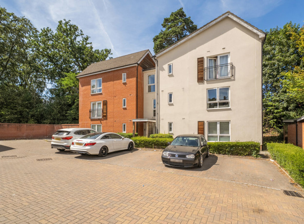 Apartment building with parked cars in front parking area.