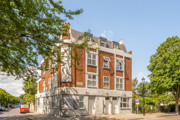 Corner view of a red brick apartment building beside a tree-lined street.
