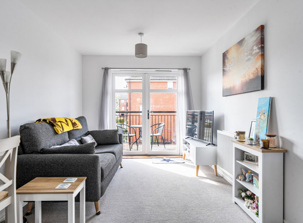 Living room with sofa, television unit and doors leading to balcony.