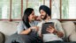 Two people relaxing on a sofa while looking at a tablet together.