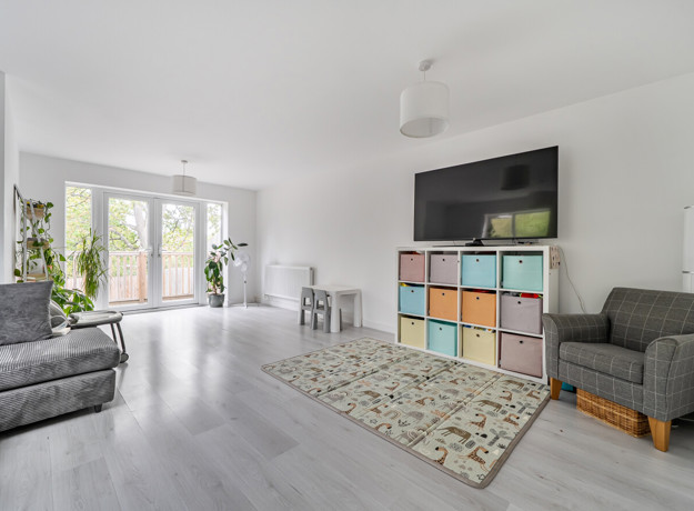 Living room with grey seating, TV, rug and patio doors to the garden.