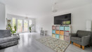 Living room with grey seating, TV, rug and patio doors to the garden.
