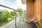 Balcony with glass railing, wooden cladding and a chair.