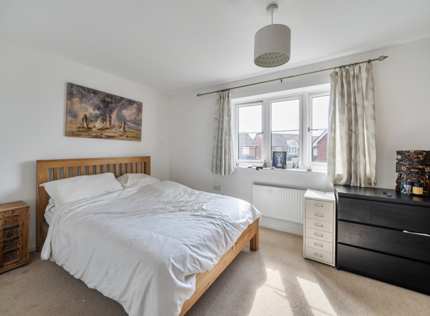 Spacious bedroom with double bed, dresser, and window letting in light.