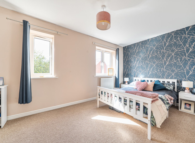 Bedroom with double bed, bedside teables, windows with curtains and patterned feature wall.