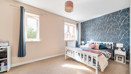 Bedroom with double bed, bedside teables, windows with curtains and patterned feature wall.